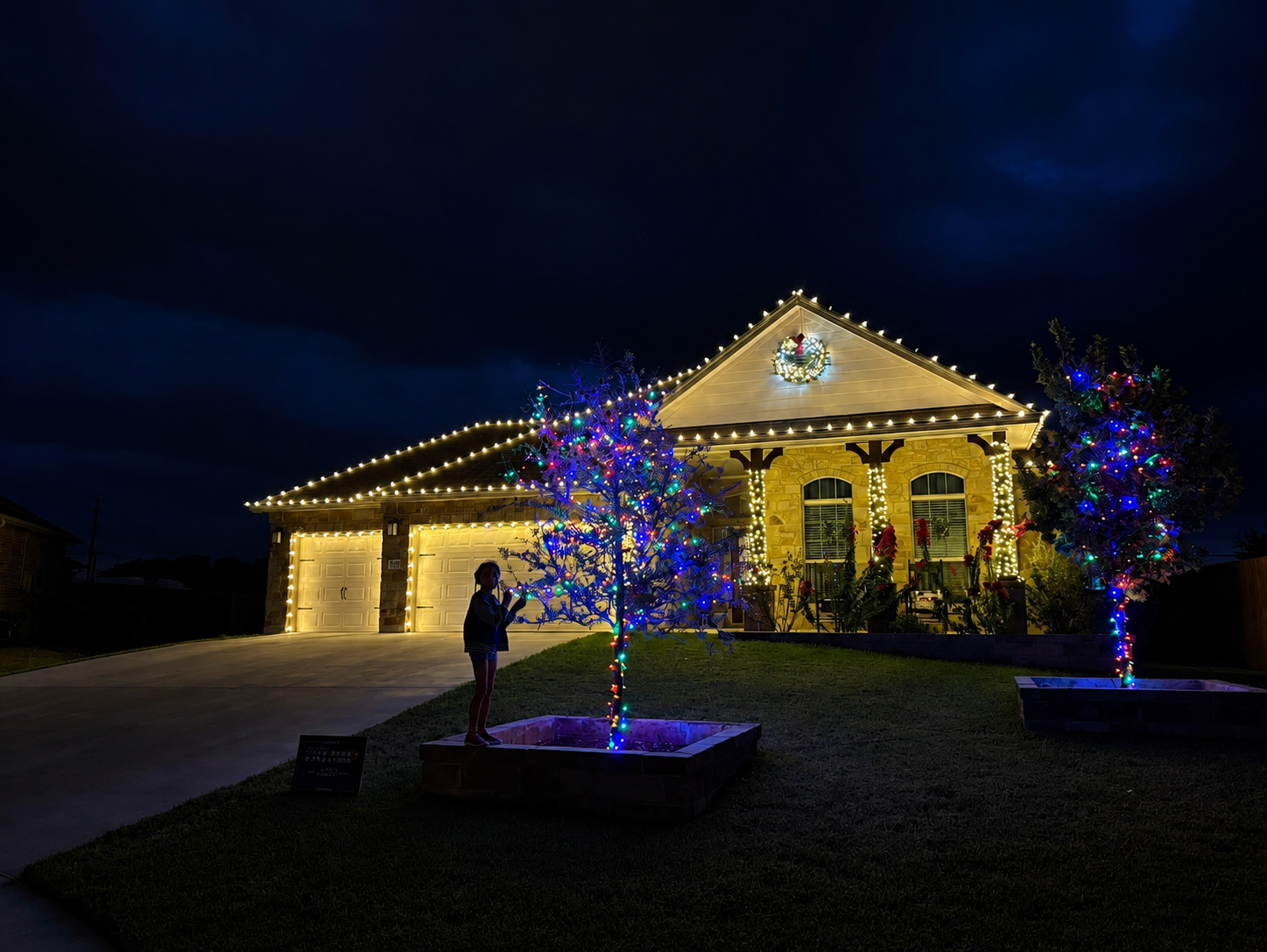 A family moment beneath colorful holiday lights at a decorated home